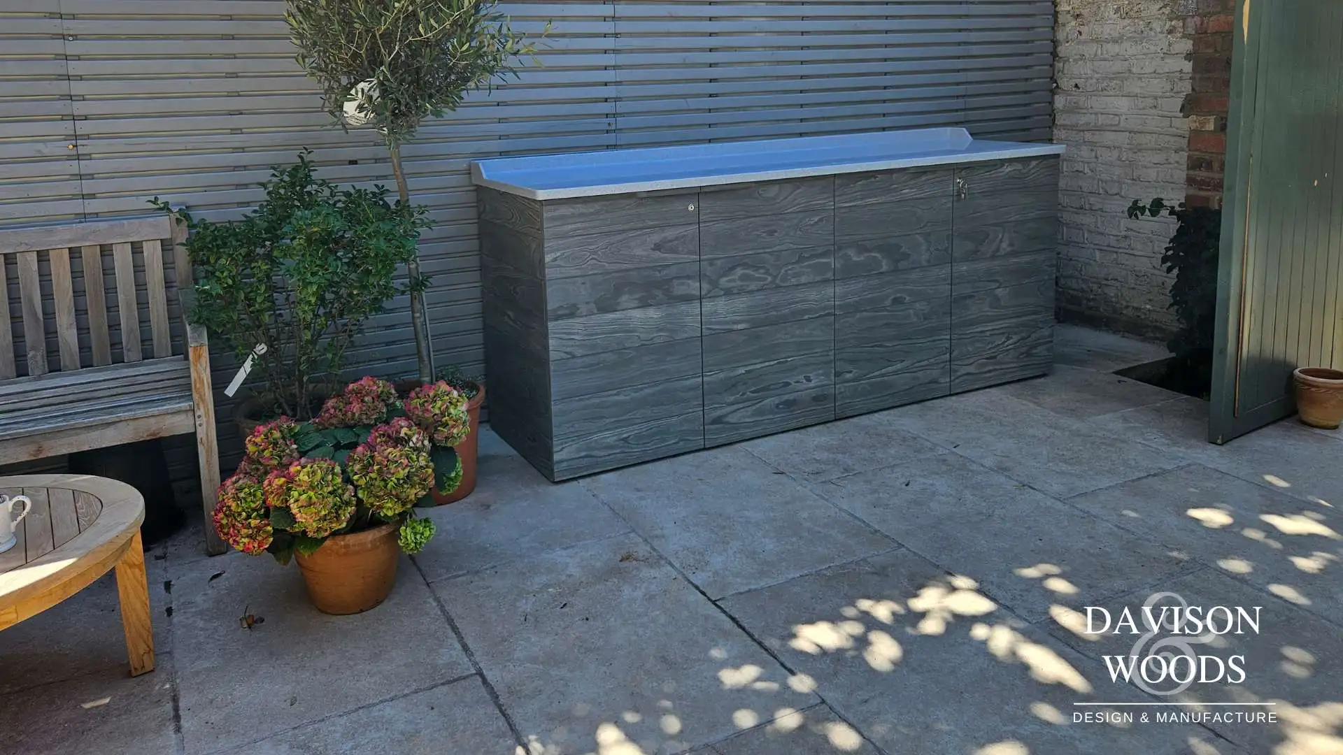 A paved patio garden area with a grey colour wooden outdoor Accoya grey Barbeque unit