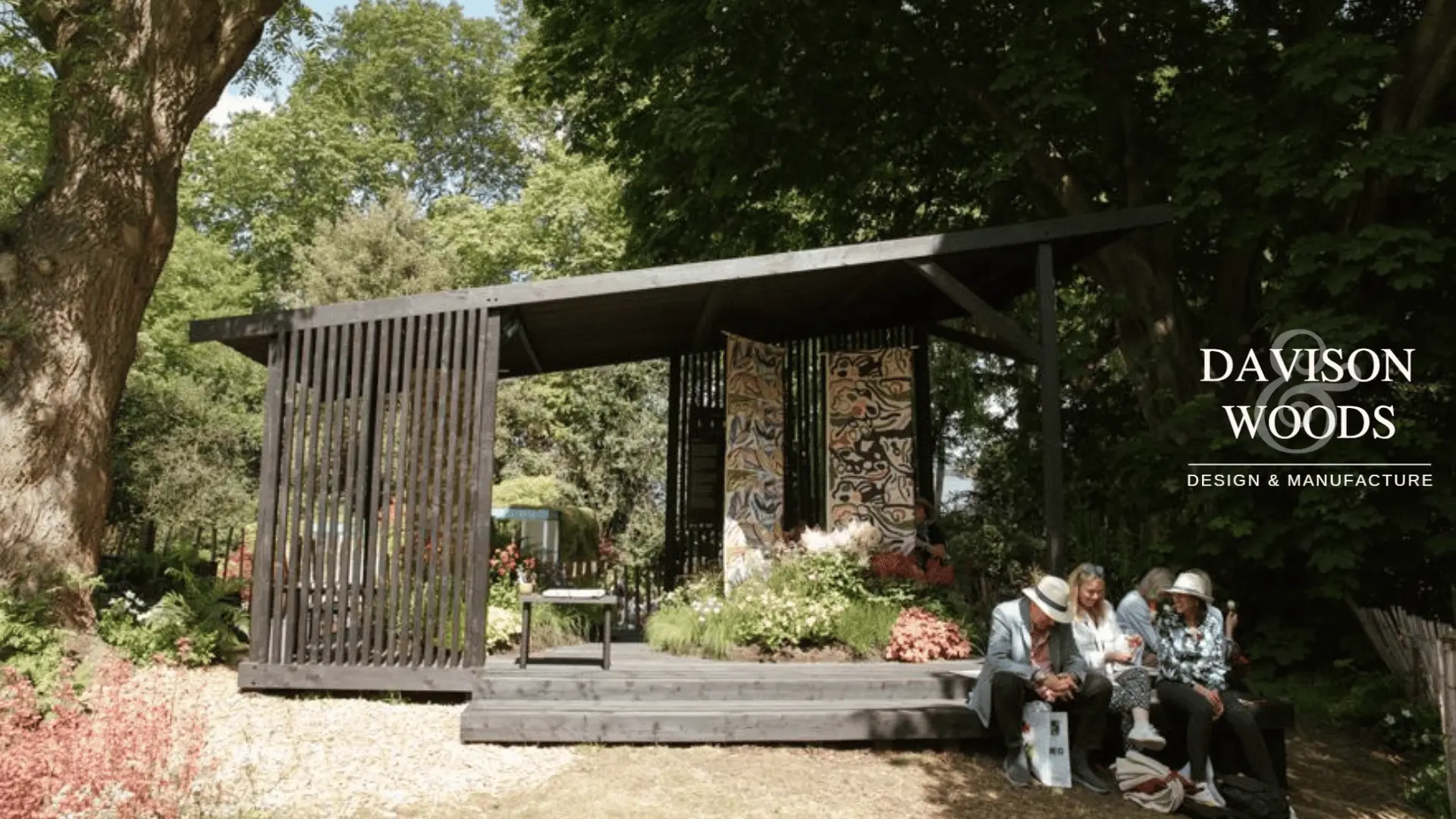 Attendees of Chelsea Flower Show sitting on edge of stand smiling and talking